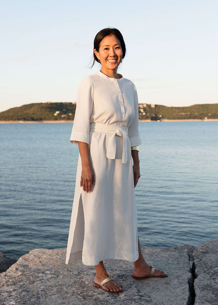 Woman wearing a Tunic style dress with pockets, a detached belt and high side slits, in white.