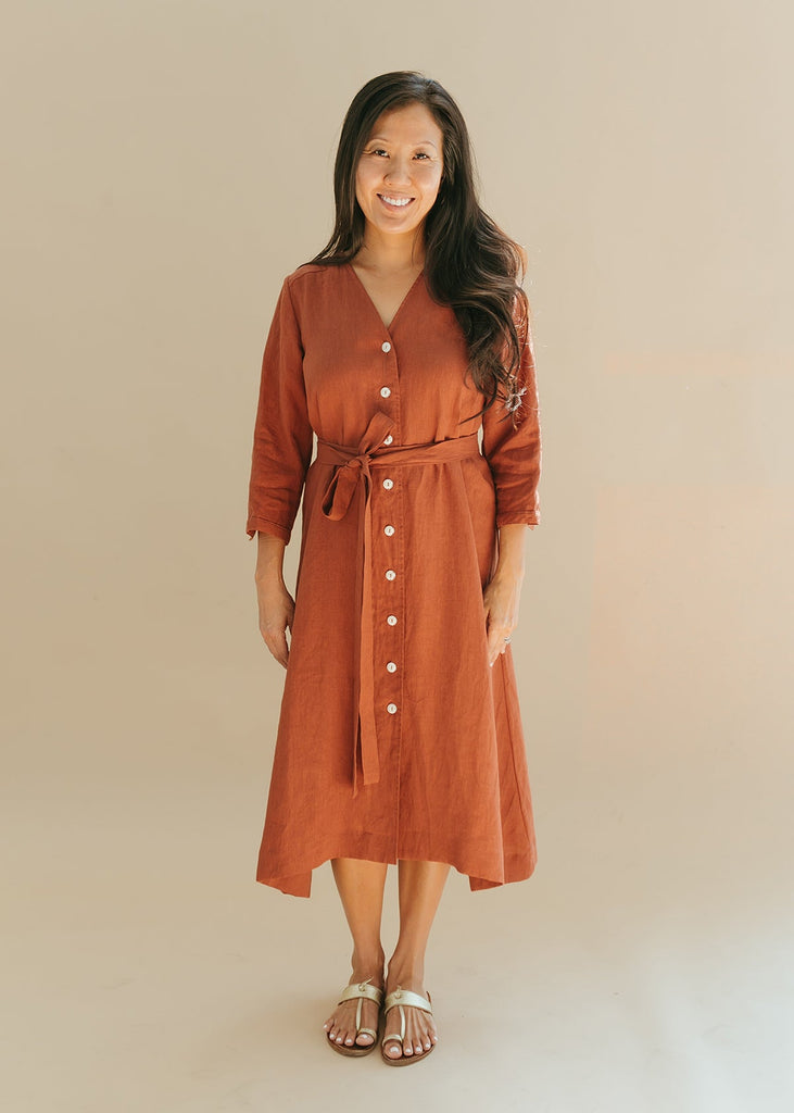 woman wearing the Sienna everyday buttoned shirtdress in burnt sienna with ¾ sleeves, a V-neck, an uneven hemline, with a belt..