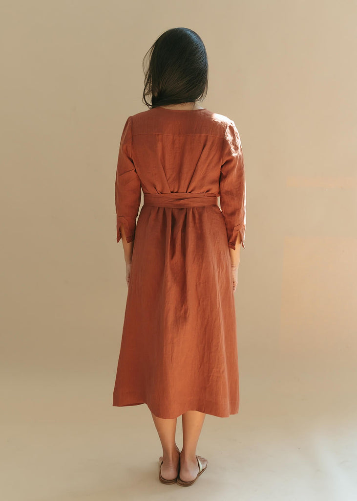 Back view of woman wearing the Sienna everyday buttoned shirtdress in burnt sienna with ¾ sleeves, a V-neck, an uneven hemline, with a belt.