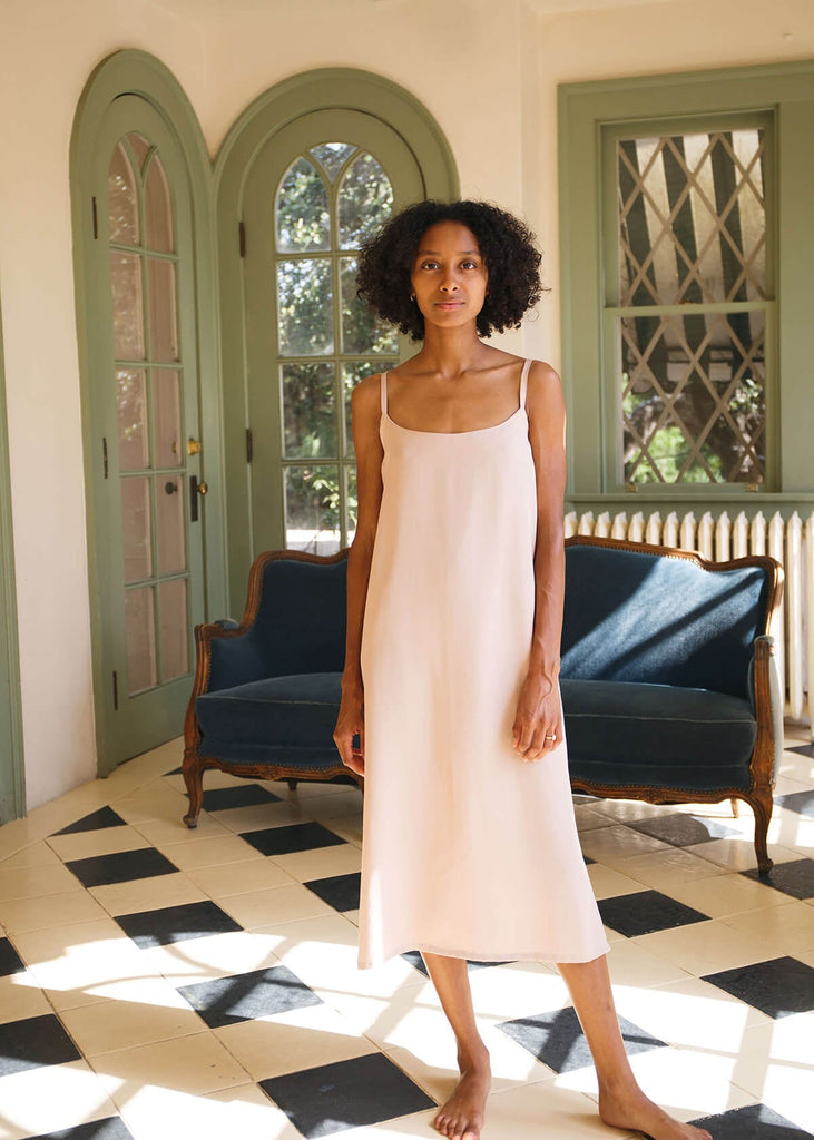  a woman wearing a blush-colored, 100% Tencel relaxed, straight fit slip dress with two side slits
