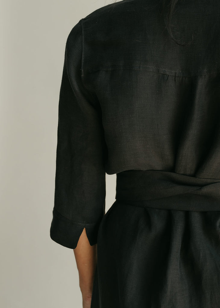 Back view of Woman wearing a Tunic style dress with pockets, a detached belt and high side slits, in black.