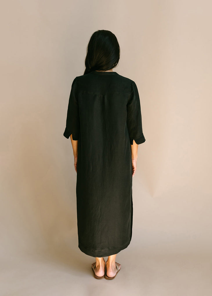 Back view of Woman wearing a Tunic style dress with pockets, and high side slits, in black.