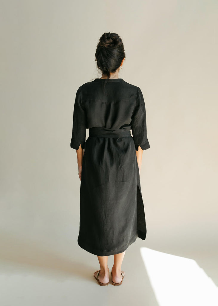 Back view of a Woman wearing a Tunic style dress with pockets, a detached belt and high side slits, in black.