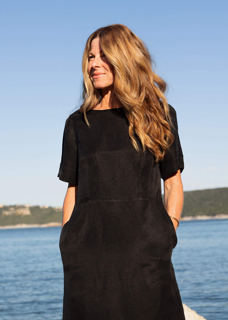 woman wearing a linen dress that hits above the knee, all black with three quarter length sleeves and two pockets.