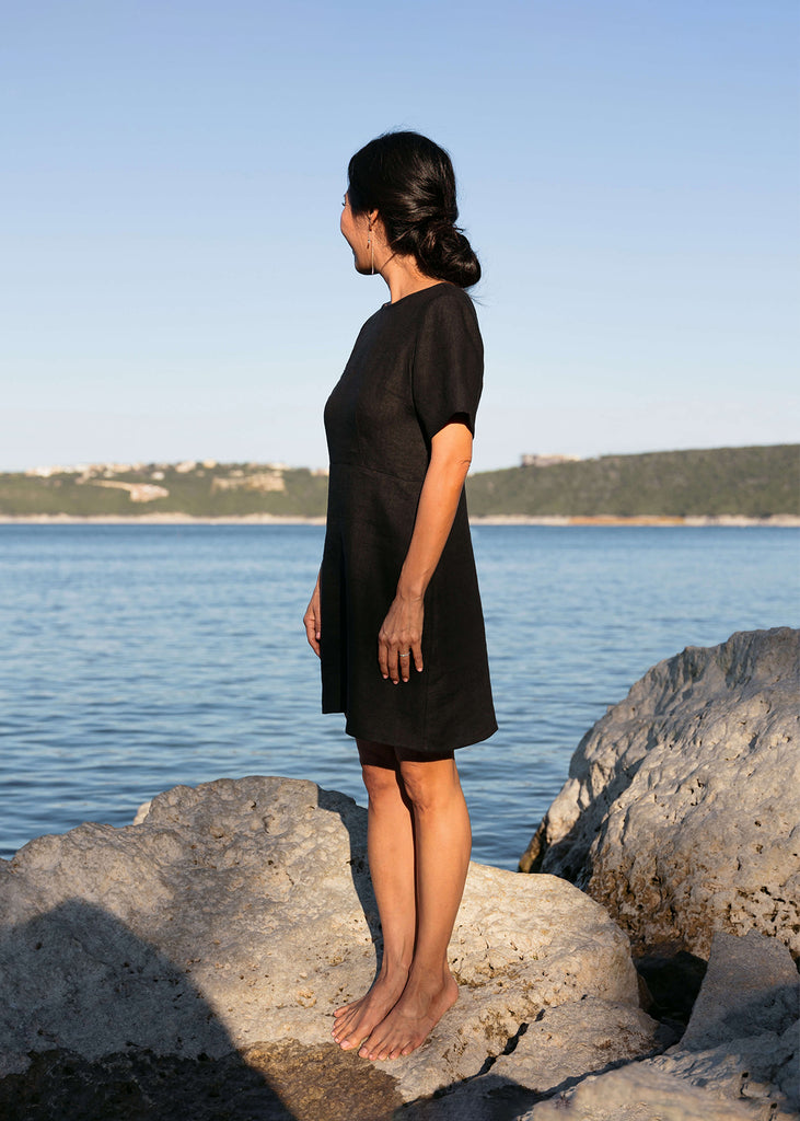 side view of woman wearing a linen dress that hits above the knee, all black with three quarter length sleeves.