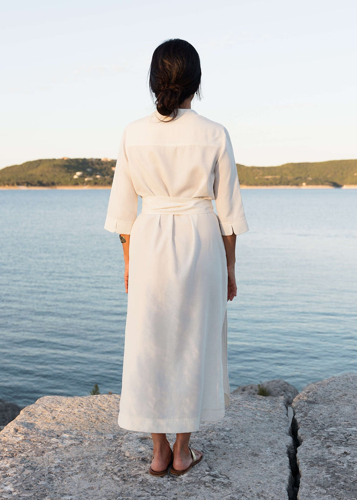 Back view of Woman wearing a Tunic style dress with pockets, a detached belt and high side slits, in white.