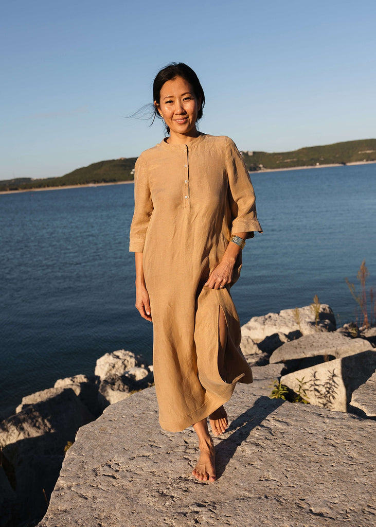 Woman wearing a Tunic style dress with pockets, and high side slits, in a light brown camel color..