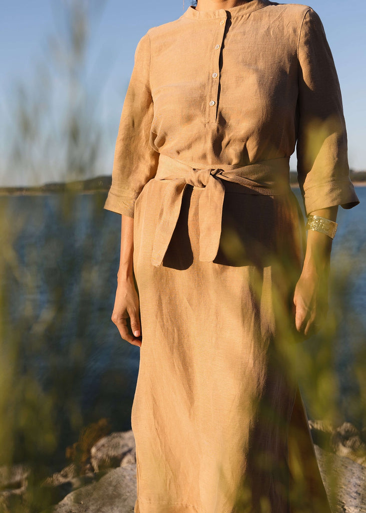 Woman wearing a Tunic style dress with pockets, a detached belt and high side slits, in a light brown camel color.