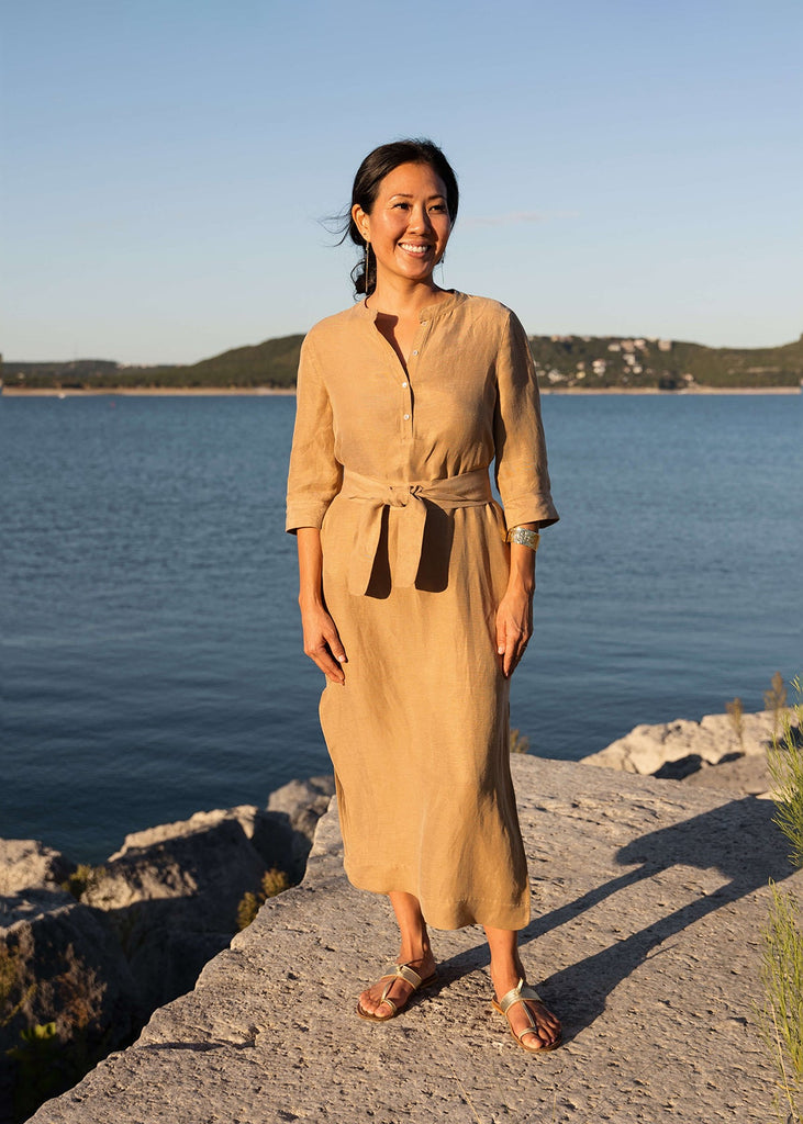 Woman wearing a Tunic style dress with pockets, a detached belt and high side slits, in a light brown camel color..