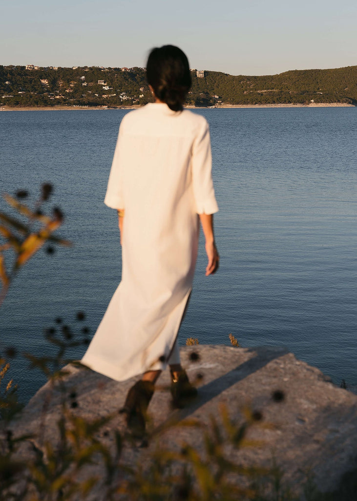 Back view of a Woman wearing a Tunic style dress with pockets,  and high side slits, in white.