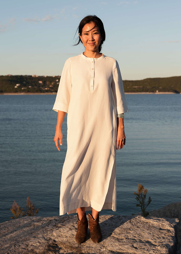 Woman wearing a Tunic style dress with pockets, and high side slits, in white.