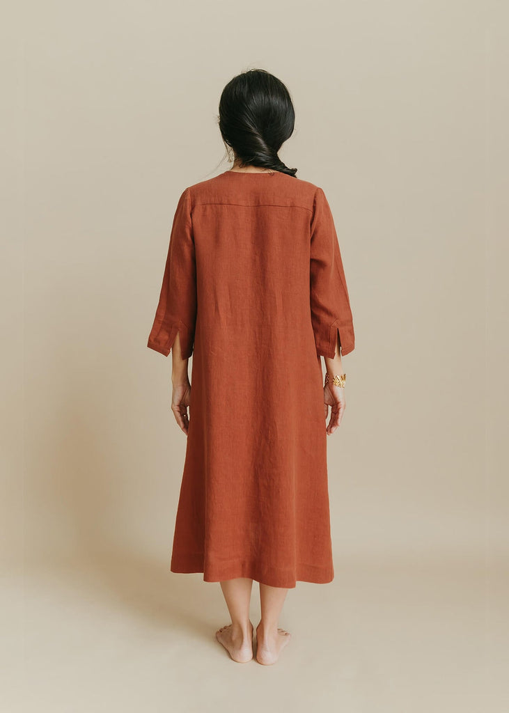 back view of woman wearing the Sienna everyday buttonedshirtdress in burnt sienna with ¾ sleeves, a V-neck, an uneven hemline.