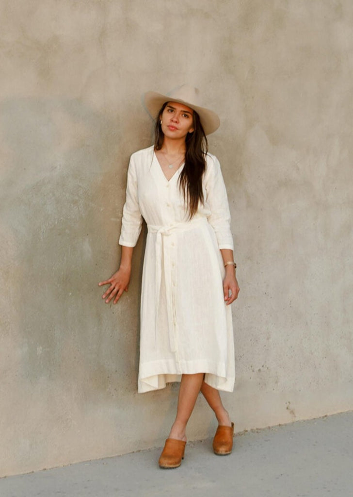 woman wearing the Sienna everyday buttoned shirtdress in white, with ¾ sleeves, a V-neck, an uneven hemline, with a belt.