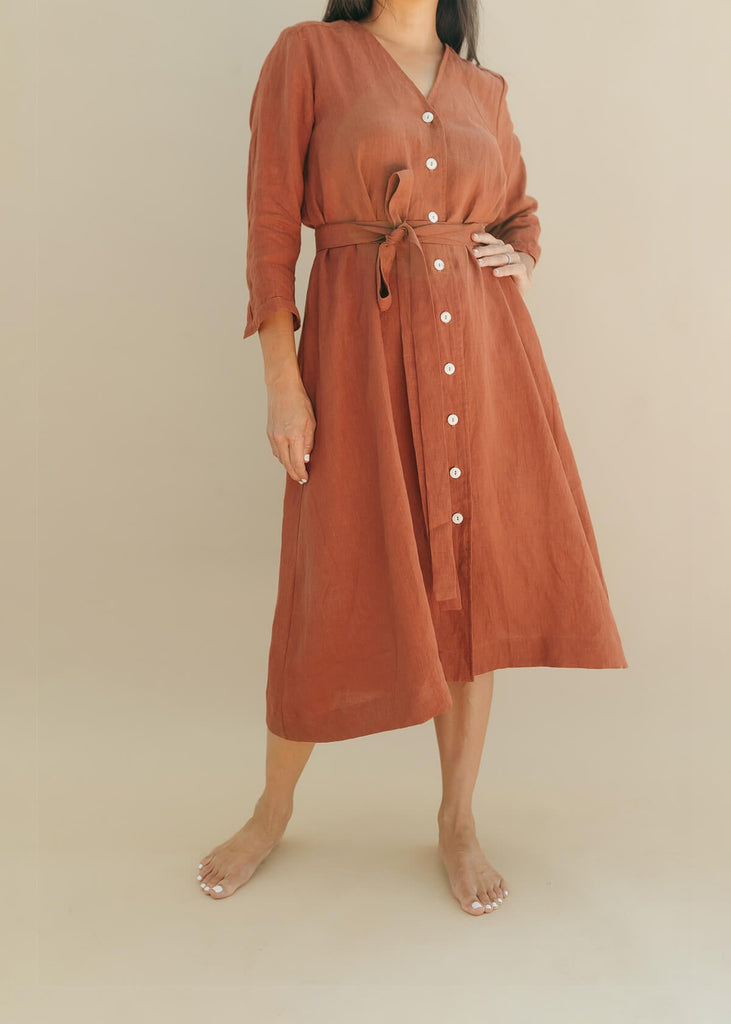 woman wearing the Sienna everyday buttoned shirtdress in burnt sienna with ¾ sleeves, a V-neck, an uneven hemline, with a belt.