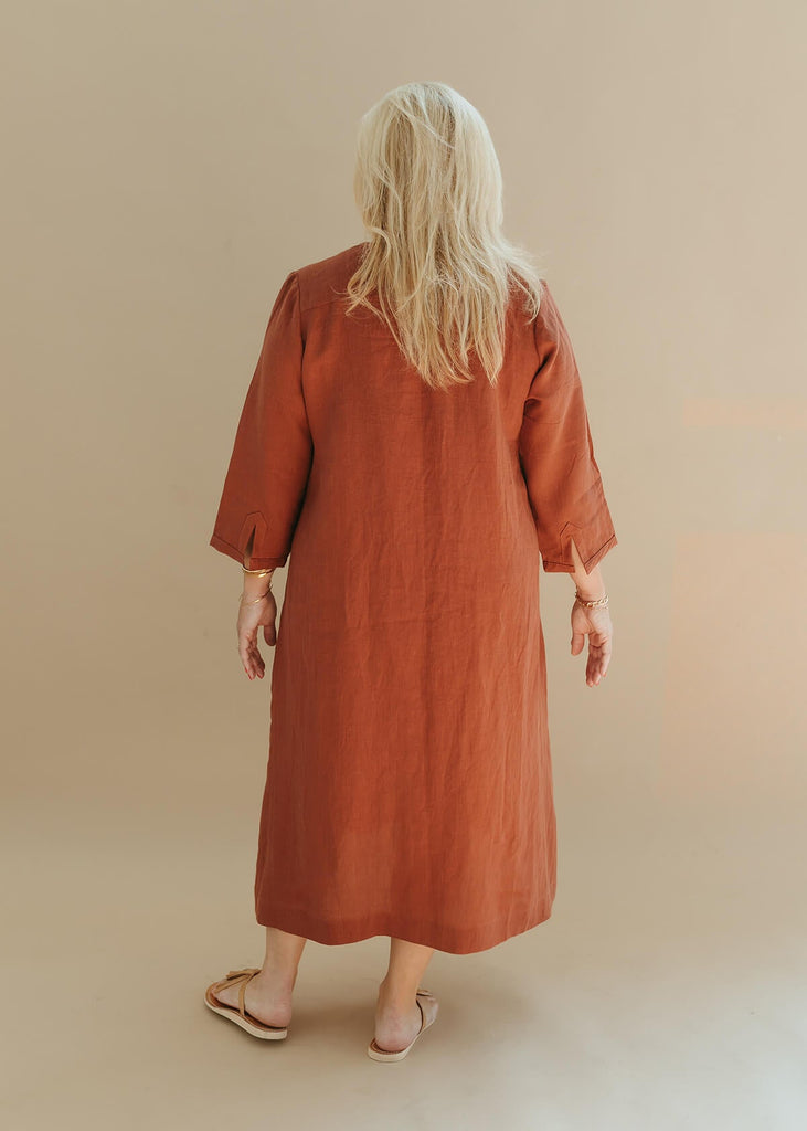Back view of a woman wearing the Sienna everyday buttoned shirtdress in burnt sienna with ¾ sleeves, a V-neck, an uneven hemline.