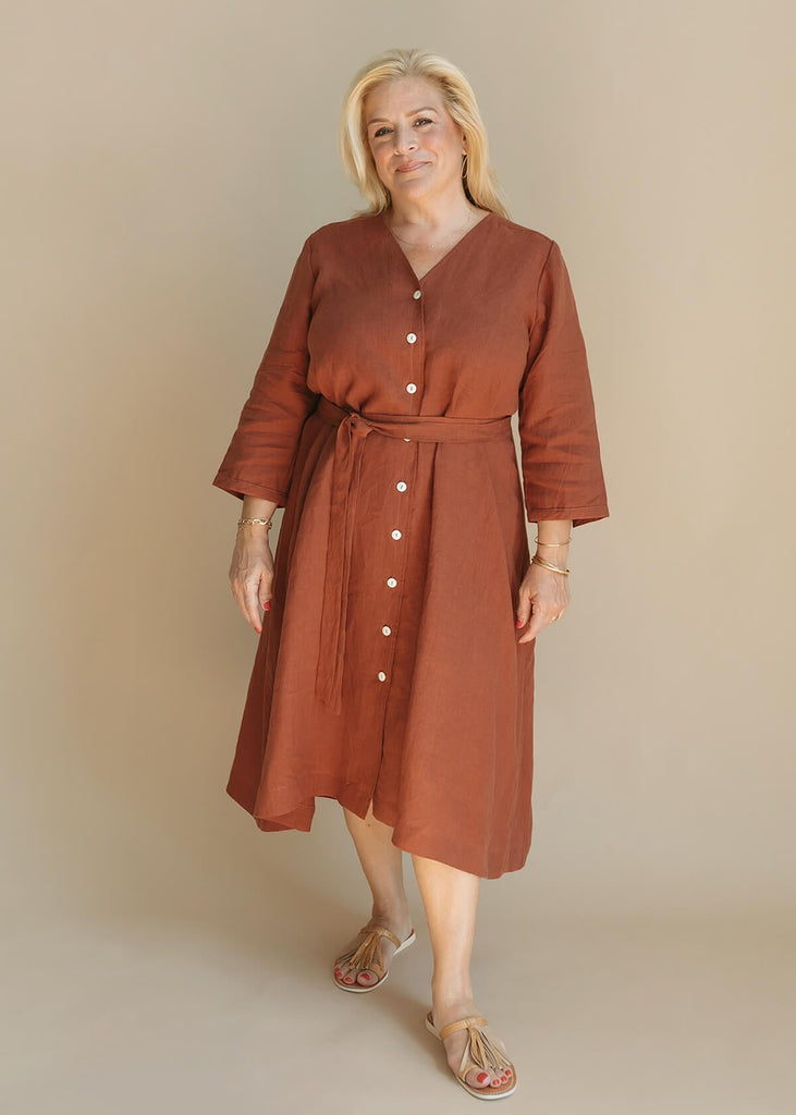 woman wearing the Sienna everyday buttoned shirtdress in burnt sienna with ¾ sleeves, a V-neck, an uneven hemline, with a belt.