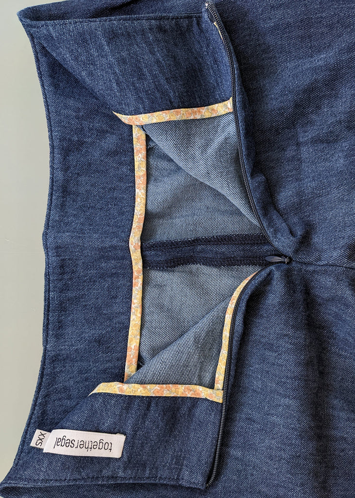 aerial view of the outside of a pair of dark blue pants, with a zipper, and a tag at the top.