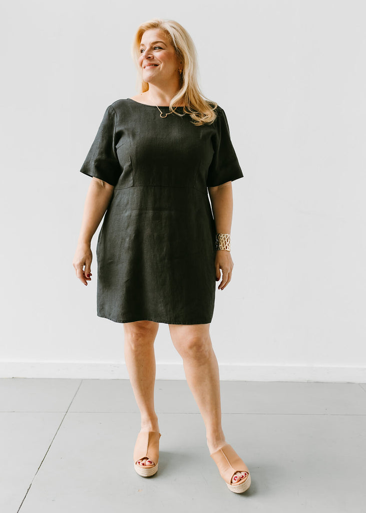 woman wearing a linen dress that hits above the knee, all black with three quarter length sleeves and slightly fitted bodice.