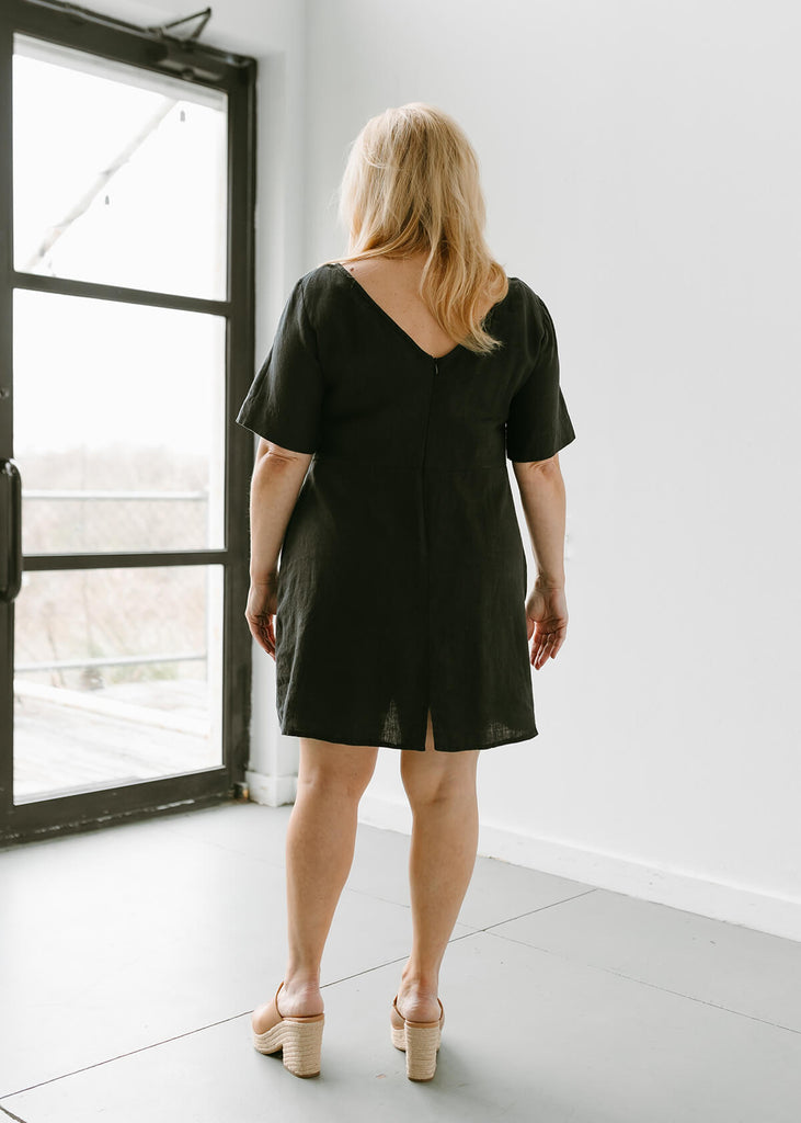 woman wearing a linen dress that hits above the knee, all black with three quarter length sleeves and zippered back.