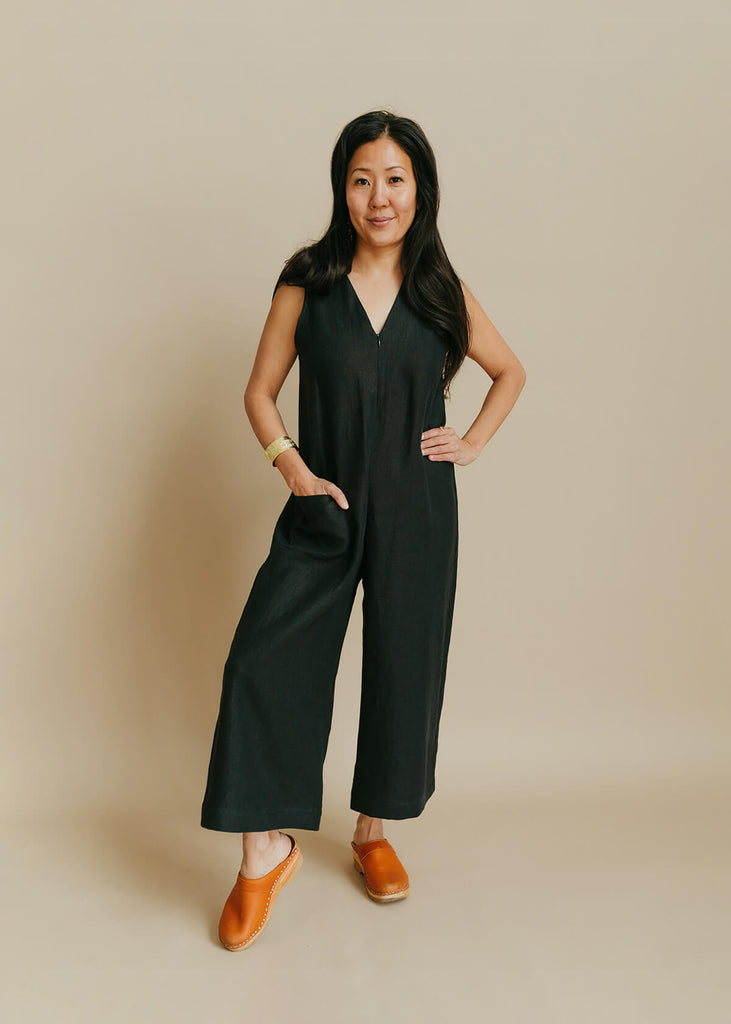 woman wearing a jumpsuit with a loose bodice with a V neck front zip opening, a detached self tie belt, one front pocket and wide cropped leg.