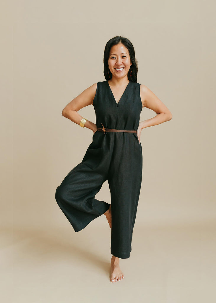 woman wearing a jumpsuit with a loose bodice with a V neck front zip opening, a detached self tie belt, one front pocket and wide cropped leg.