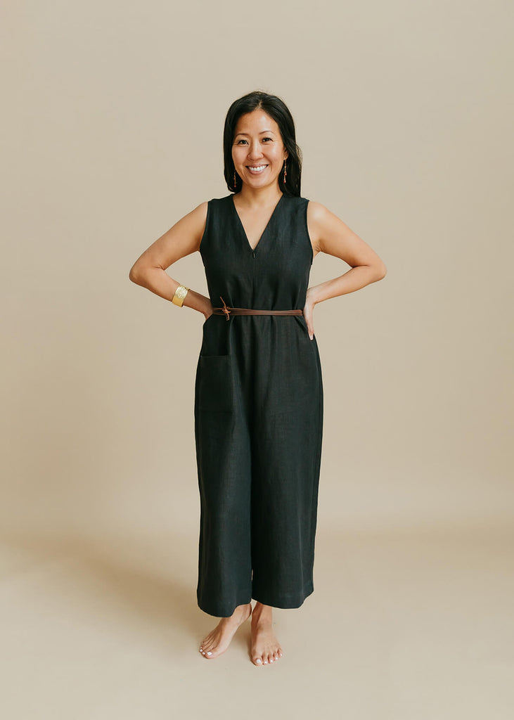 woman wearing a jumpsuit with a loose bodice with a V neck front zip opening, a detached self tie belt, one front pocket and wide cropped leg.