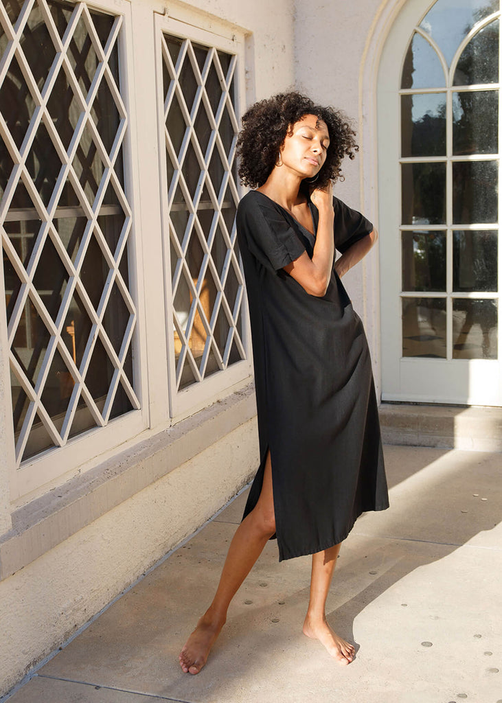 woman wearing a knee length black dress with v-neck, three-quarter length sleeves, and a slit on the side.