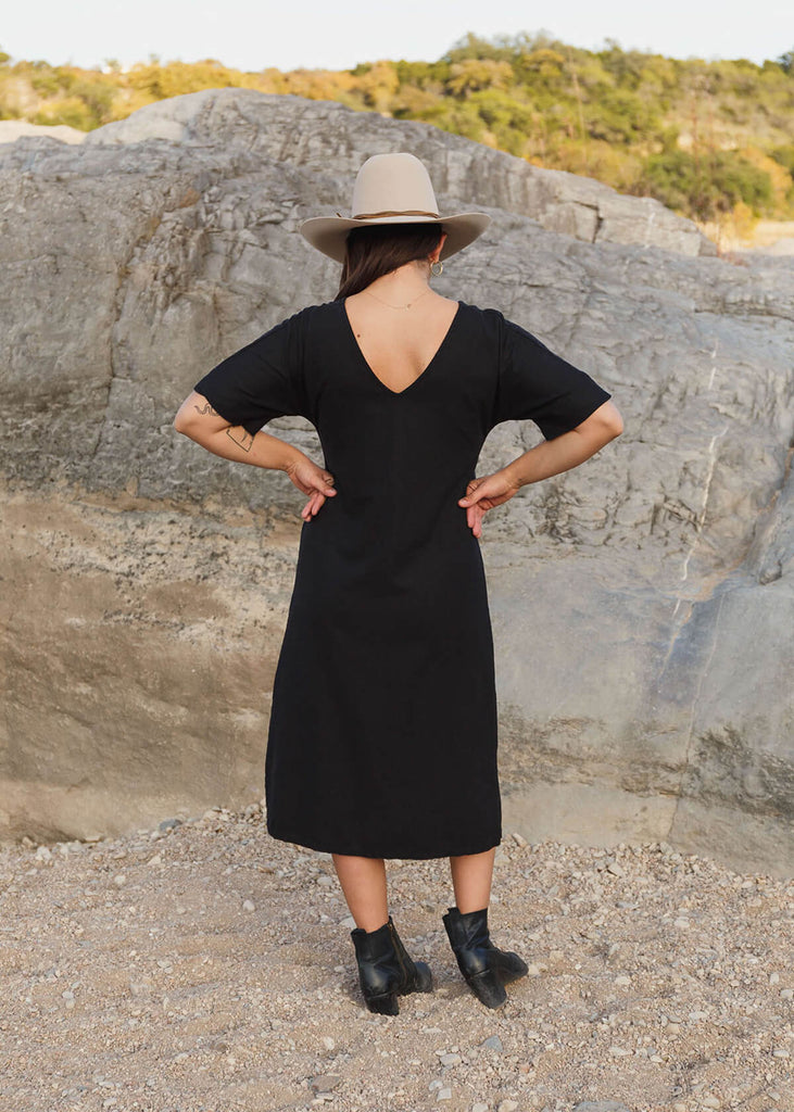 back of woman, wearing a mid-calf length black dress with three-quarter length sleeves. 