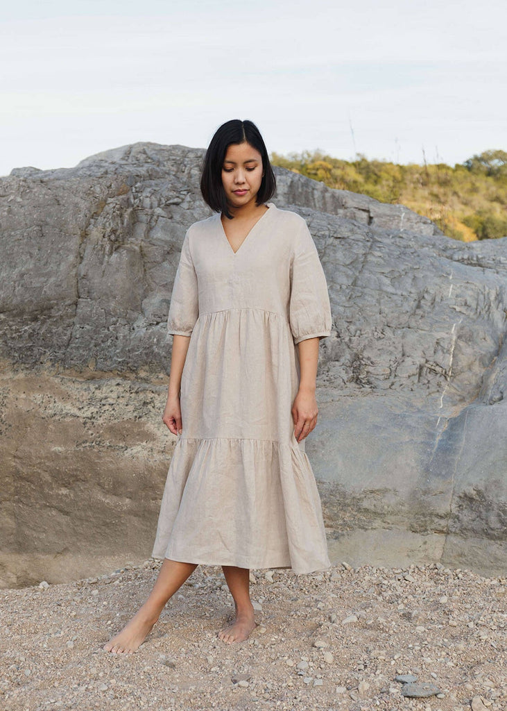  A woman wearing a 100% Japanese linen tiered dress with a loose fit and gathering at the waist, in a natural color.