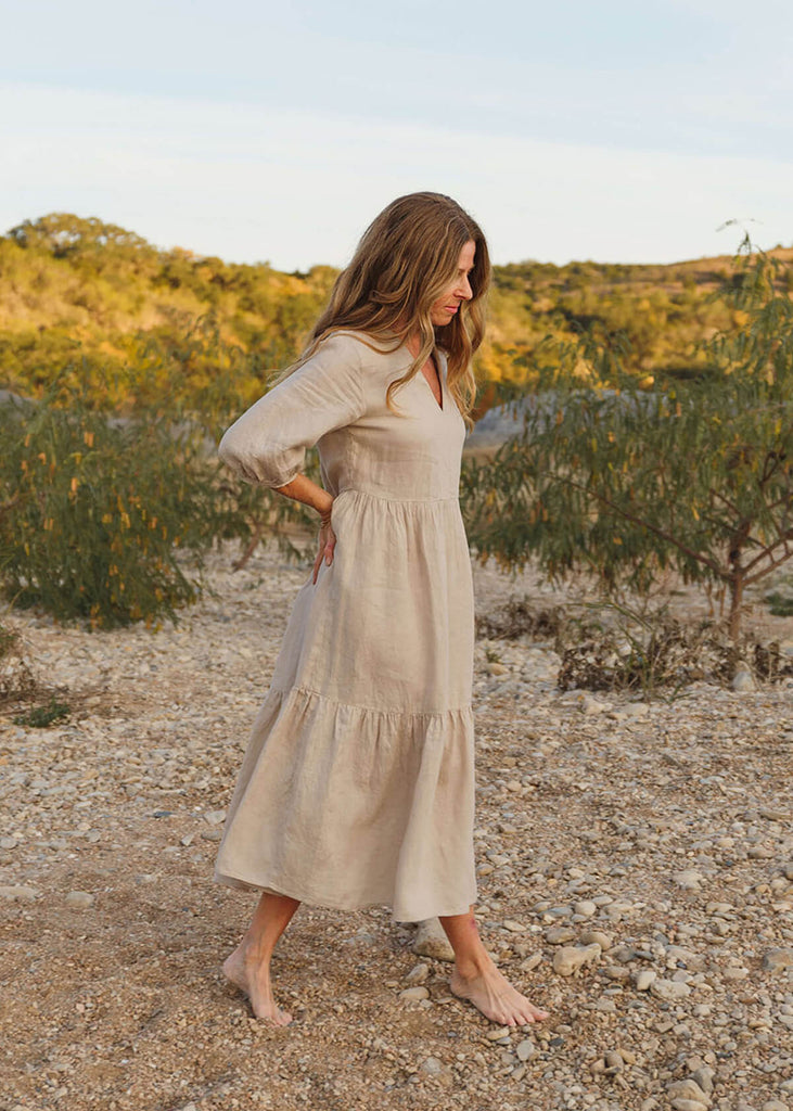 Side view of  A woman wearing a 100% Japanese linen tiered dress with a loose fit and gathering at the waist, in 