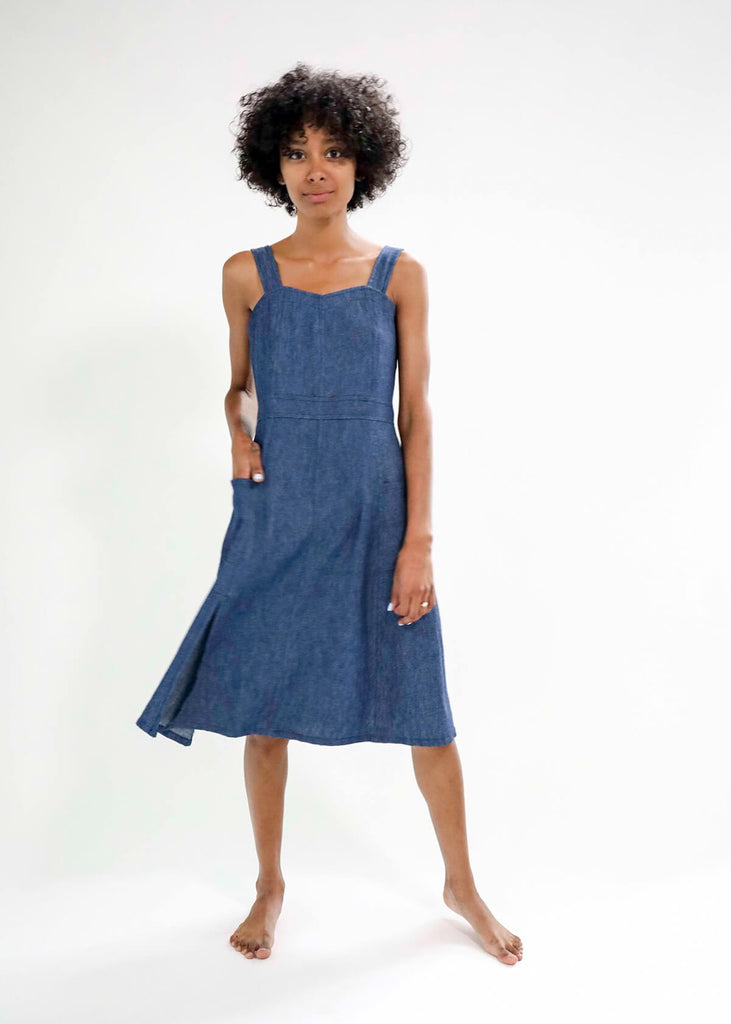 woman wearing a blue sundress with a fitted bodice and flattering A-line skirt; adjustable button straps, two pockets, one side slit.