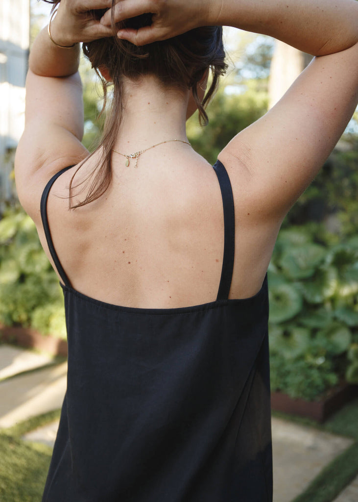 back view of a woman wearing a black, 100% Tencel relaxed, straight fit slip dress with two side slits