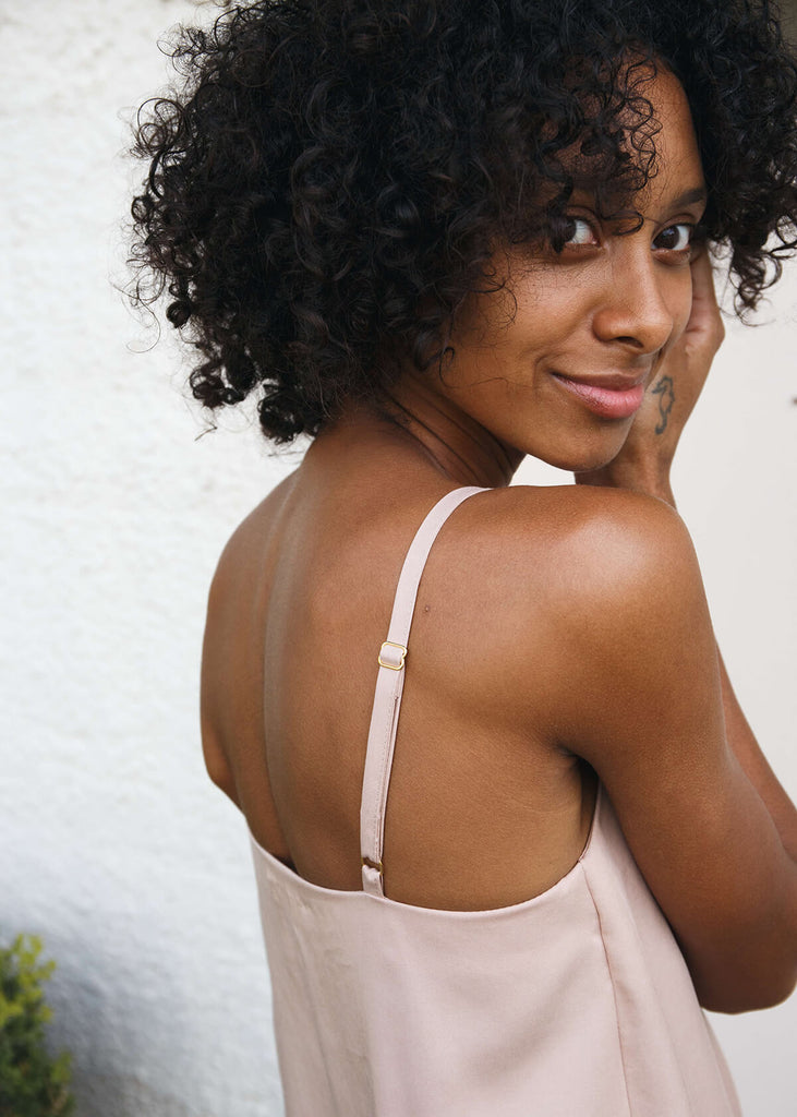 back side view of  a woman wearing a blush-colored, 100% Tencel relaxed, straight fit slip dress with two side slits