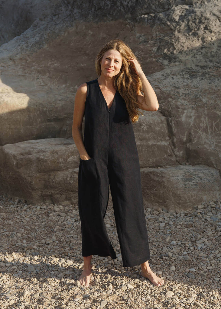 woman wearing a linen jumpsuit with a loose bodice with a V neck front zip opening, a detached self tie belt, one front pocket and wide cropped leg.