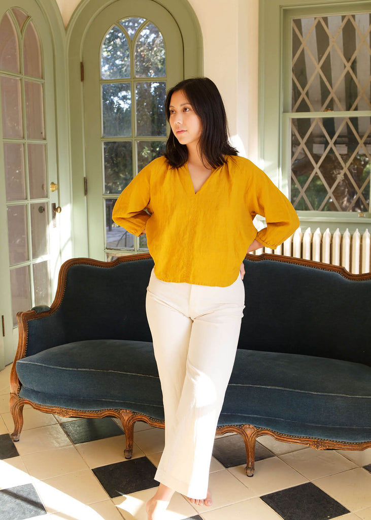 woman wearing ivory colored, high-waisted, wide-leg pants with a slight ankle crop, single button front closure, and back pockets.