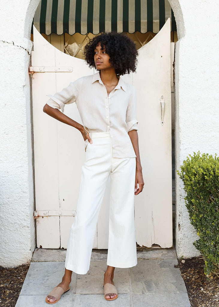 woman wearing white high-waisted, wide-leg pants with a slight ankle crop, single button front closure, and back pockets.
