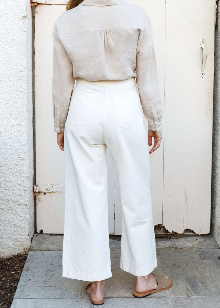 back view of woman wearing white high-waisted, wide-leg pants with a slight ankle crop, single button front closure, and back pockets.
