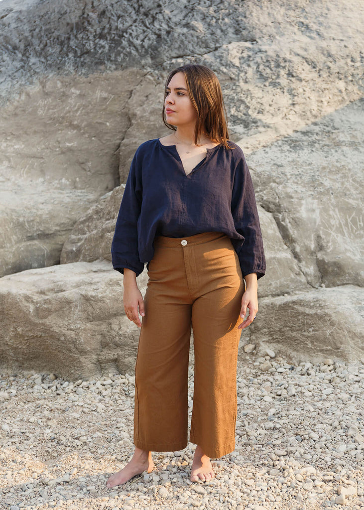 woman wearing brown high-waisted, wide-leg pants with a slight ankle crop, single button front closure, and back pockets.