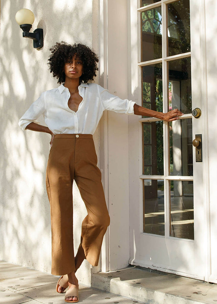 woman wearing brown high-waisted, wide-leg pants with a slight ankle crop, single button front closure, and back pockets.