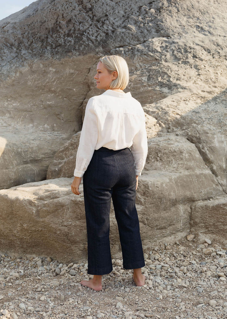 back view of woman wearing a very dark blue wide-leg, slightly cropped pant with no pockets, and Zipper and single button front closure.