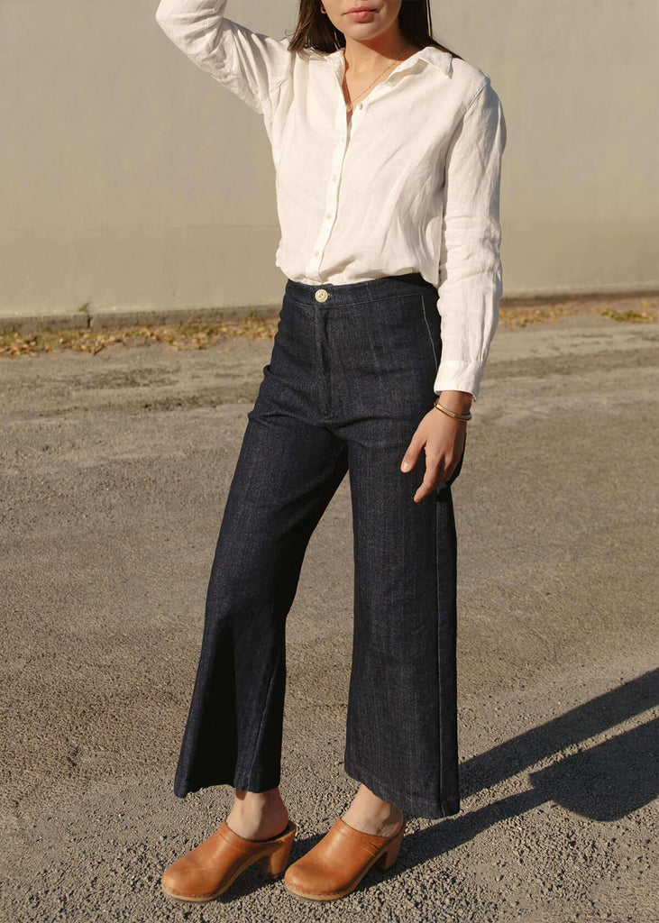 side view of a woman wearing a very dark blue wide-leg, slightly cropped pant with no pockets, and Zipper and single button front closure.