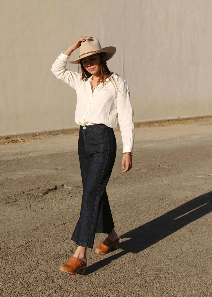 side view of a woman wearing a very dark blue wide-leg, slightly cropped pant with no pockets, and Zipper and single button front closure.