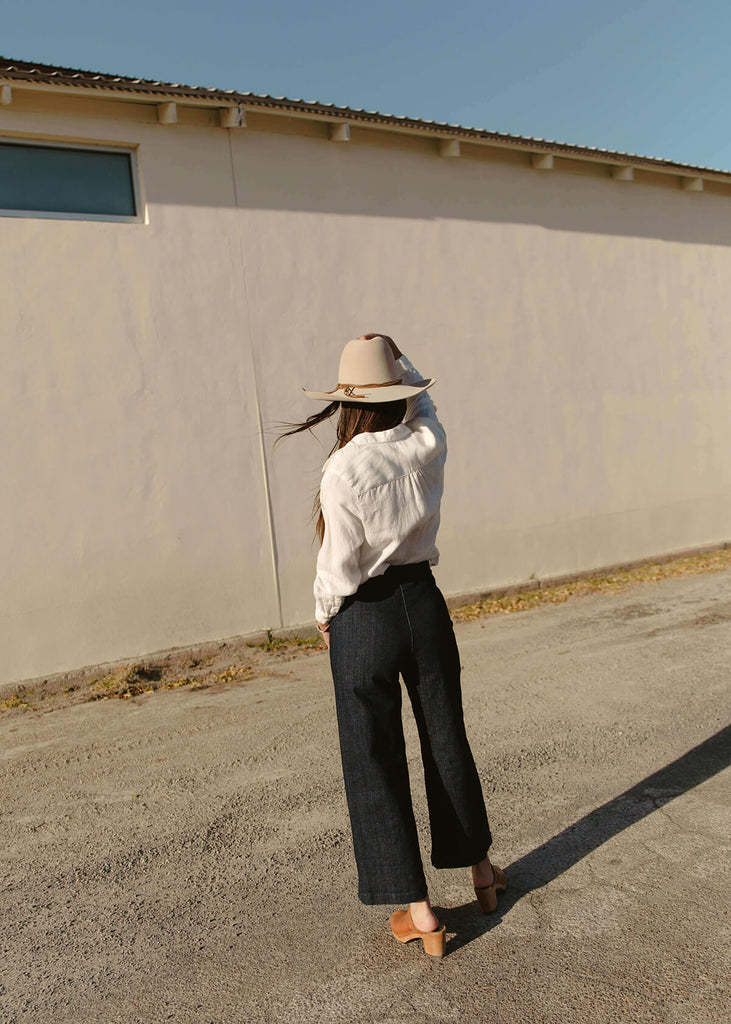 back view of woman wearing a very dark blue wide-leg, slightly cropped pant with no pockets, and Zipper and single button front closure.