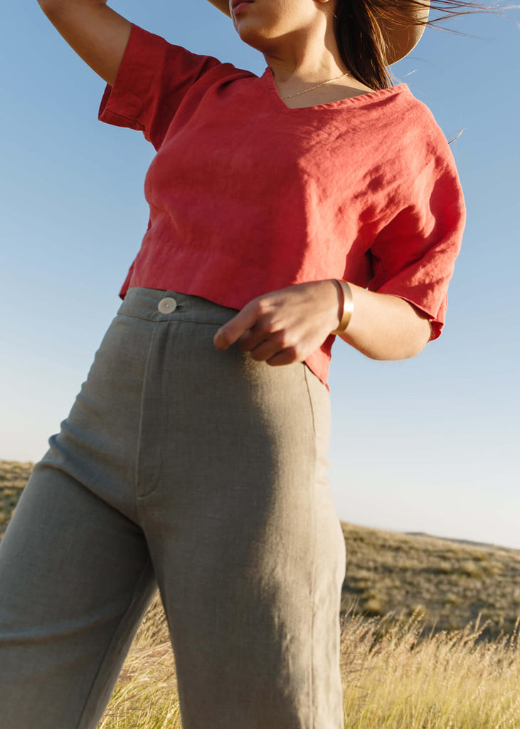 woman wearing high-waisted, natural colored pants, with a single button front closure.