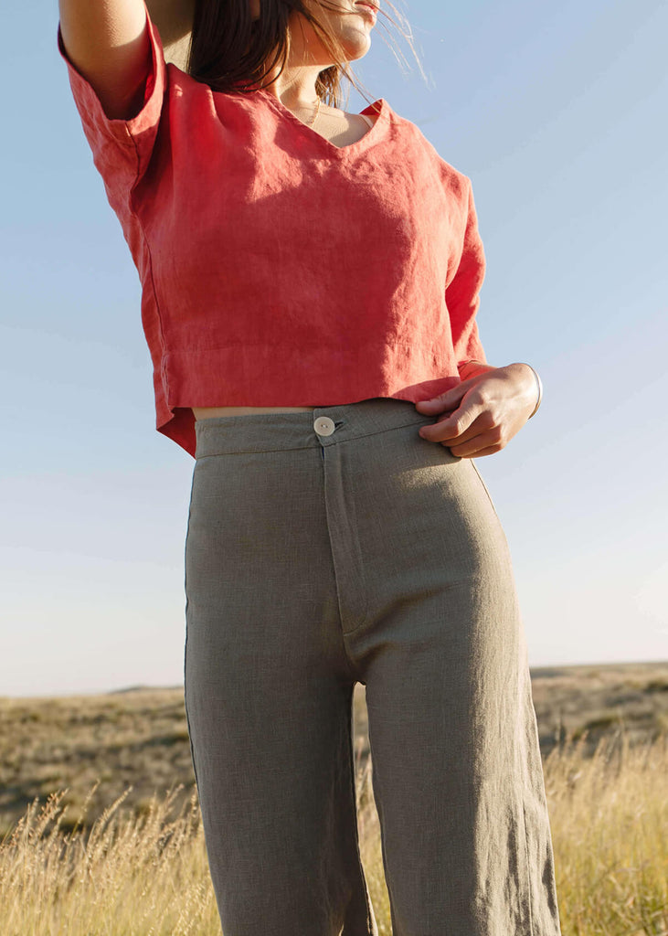woman wearing high-waisted, natural colored pants, with a single button front closure.