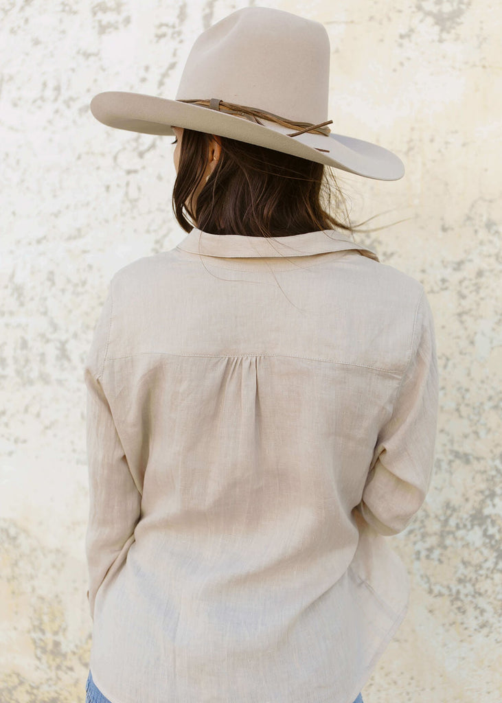 back view of woman wearing a linen natural cream-colored button up shirt.