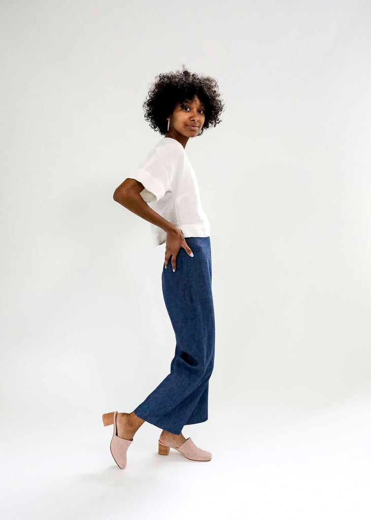 side view of a Woman wearing a boxy crop top with V neck front, relaxed dropped shoulder sleeves, two inch hems and two small side slits, in white.