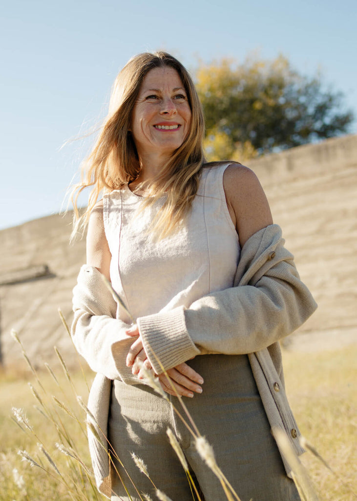 Woman wearing a reversible linen sleeveless crop top in white, with princess seams, small slit on side front, V in back. 