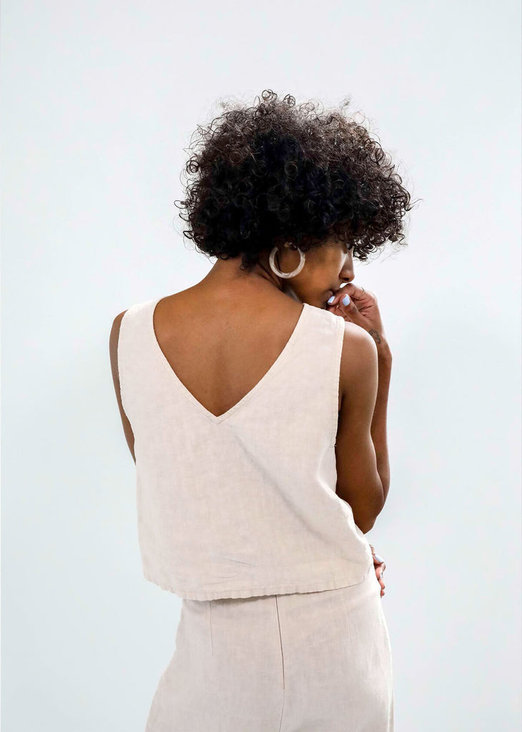 back view of a woman wearing a reversible linen sleeveless crop top in white, with princess seams, small slit on side front.
